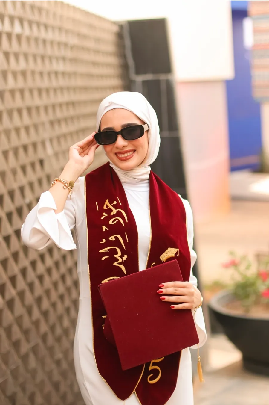 خرّيجة بنظّارة شمسية تحمل قبّعة التخرّج وحافظة الشهادة في لقطة مرحة